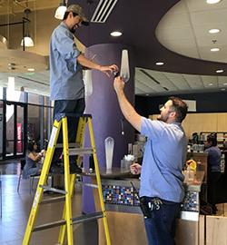 赌博平台 facility employee giving a light bulb to another 赌博平台 facility employee on a ladder.